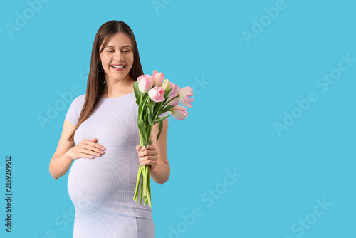 Young pregnant woman with tulips on blue background