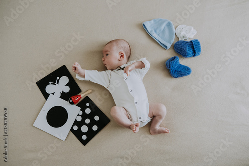 Cute 1 month baby boy lying among various playful colorful toys on beige blanket. Newborn surrounded by vivid objects participating actively in sensory exploration and learning. 