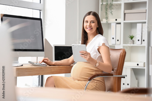 Young pregnant businesswoman with tablet computer and calculator working at t...