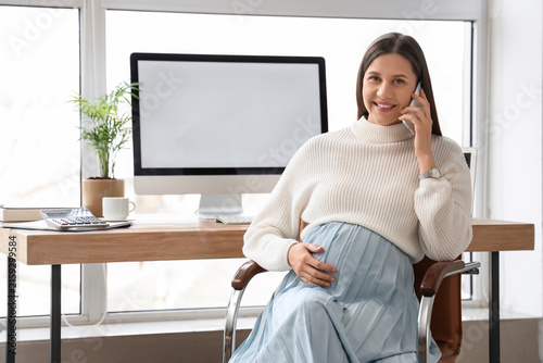 Young pregnant businesswoman talking by mobile phone in office