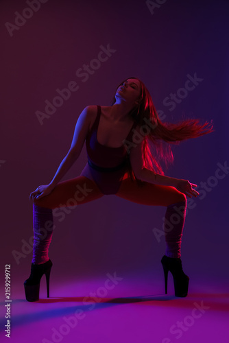 Beautiful young woman in high heels dancing on dark purple background