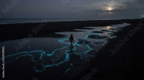 Woman Traveler Exploring a Glowing Bioluminescent Shore at Night