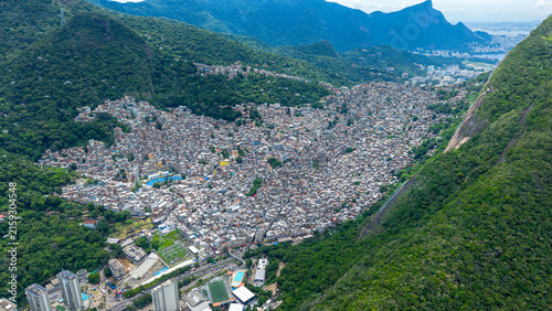 Aerial view of the dense urban landscape of Rocinha, featuring tightly packed residential buildings nestled between lush green mountains in Rio de Janeiro, Rio de Janeiro, Brazil.