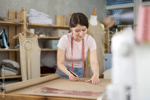Foto Young female seamstress drawing pattern on paper in sewing workshop