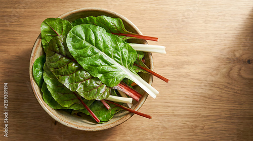 Fresh Swiss chard leaves in a ceramic bowl on a wooden table, top view.