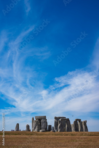 The prehistoric megalithic structure Stonehenge during a summer afternoon with dry, brown grass in the foreground