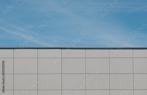 Minimalist modern building facade with gray metal panels beneath a blue sky