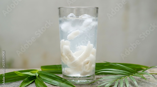 Young coconut ice is served in a clear glass against a gray background.