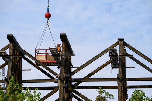 Cuadro en lienzo Workman in safety equipment in work basket help aloft by crane, old wood railway