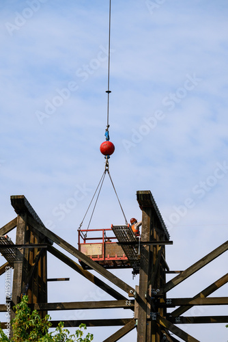 Obraz na plátne Workman in safety equipment in work basket help aloft by crane, old wood railway