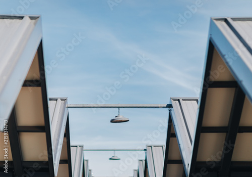 Geometric metal canopy structures with hanging lamps against a blue sky
