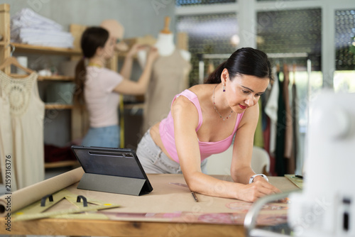 Fotografie Experienced female tailor drawing clothing outlines on paper in sewing studio