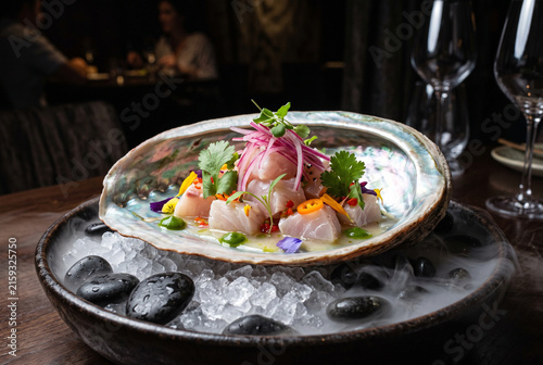 Elegant fine dining raw fish ceviche served in abalone shell with dramatic dry ice smoke over ice