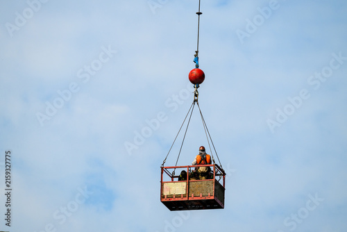 Construction workers in safety gear in arial work basket high up against a sunny blue sky, summer work project in America
