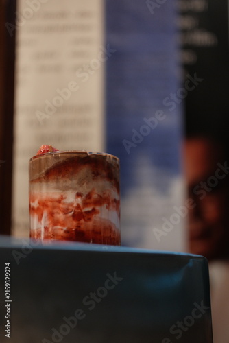 Glass of layered strawberry dessert with cream and fruit topping on a dark surface