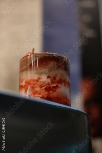 Layered dessert in a glass cup with red fruit sauce and cream topping