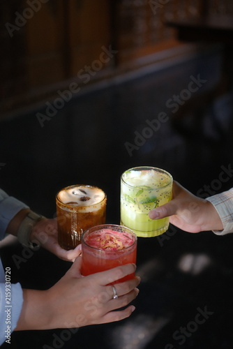 Friends toasting with colorful iced cocktails and coffee drinks in a dark cafe setting