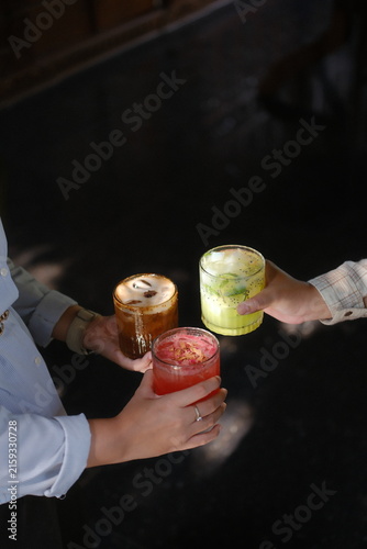 Friends holding colorful cocktails for a toast at a dark bar counter