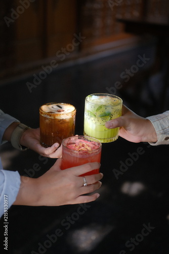 Two people toasting with colorful layered cocktails in dimly lit bar setting