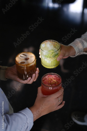 Close-up of hands clinking colorful layered cocktails in stylish bar setting