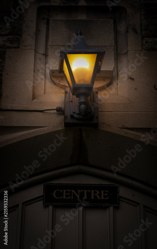 Vintage glowing lantern mounted on stone wall above wooden door with Centre sign