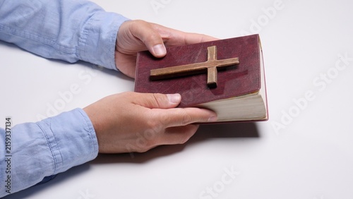 Fotografie Person's hands gently holding a closed bible with a small wooden cross resting o