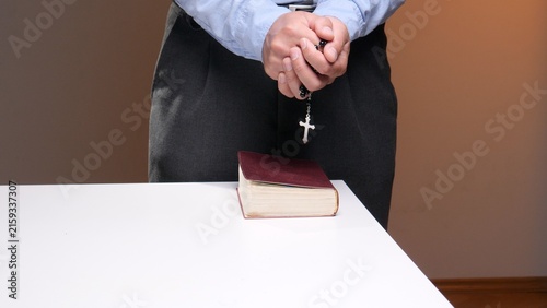 Obraz na płótnie Person's hands clasped in prayer while holding a rosary with a crucifix, standin