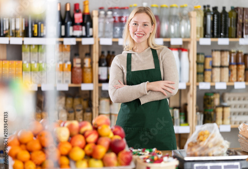 Konstfotografi Portrait of positive female seller behind the counter of a grocery store