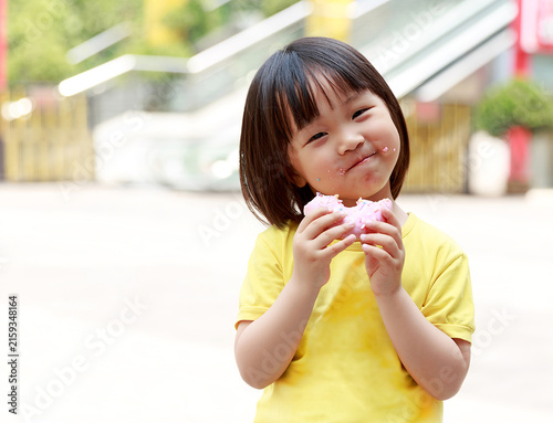 Foto Happy Little Asian Girl Eating Pink Glazed Donut with Crumbs on Face, Sweet Snac