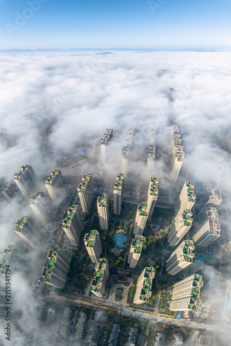 Aerial view of dense high-rise residential buildings rising above a thick layer of clouds under a clear blue sky.