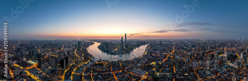 Photography A wide panoramic aerial view of a sprawling urban city with a winding river, illuminated buildings and roads, at dawn with a clear sky