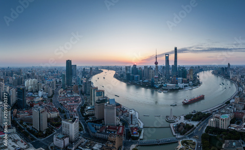 Photography A panoramic dawn view of a bustling city along a winding river, with tall skyscrapers and vessels on the water