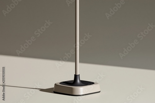 Close up of a beige floor lamp base with a thin metal pole on a light surface with shadow cast