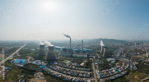 Canvas Print Aerial shot of a large thermal power plant with cooling towers and smokestacks, adjacent to urban and suburban areas under clear sky