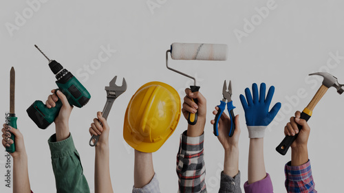 Diverse Hands Holding Up Various Tools and Safety Gear Against a Neutral Background hard hat