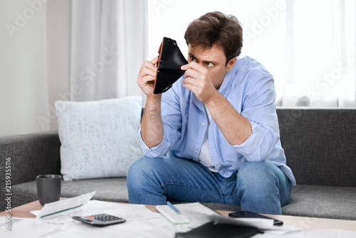 Stressed man looks into an empty wallet, struggling with unpaid utility bills, rising heating expenses, and financial crisis due to inflation.