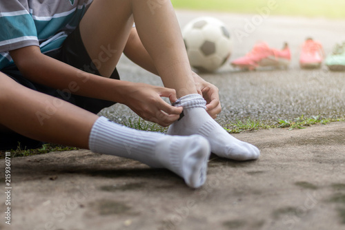 Close-up of a young soccer player pulling up white socks before football training outdoors.