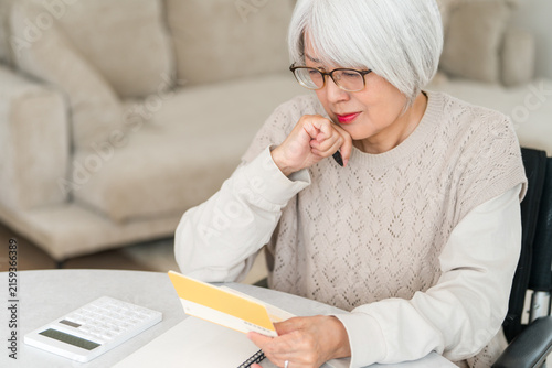 Quadro su tela A senior woman uses a calculator to perform calculations (for retirement funds, living expenses, and pension) while looking at her savings passbook