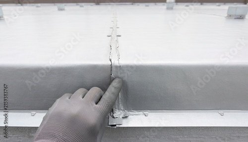 Gloved technician hand inspecting the lap seam integrity and joint sealing on a commercial flat roof membrane
