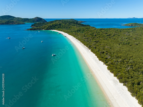 Aerial view of Whitehaven Beach with its pristine white sand and turquoise water surrounded by lush forest and boats in the Whitsunday Islands, Airlie Beach, Queensland, Australia.