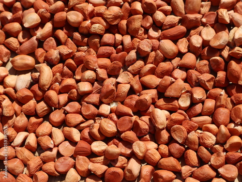 Raw shelled peanuts spread across a surface, showing whole and split peanut kernels with their natural reddish-brown skins and varied shapes.