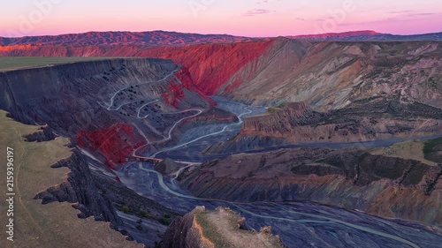 Aerial view of a deep gorge with a winding river and red cliffs at sunset in Anjihai Grand Canyon, Xinjiang, China