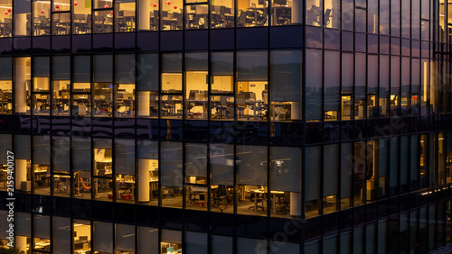 Aerial view of the illuminated glass facade of a modern office building with visible workspaces at dusk in Gdansk, Poland.