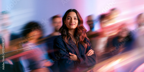 Smiling Female Indian American Businesswoman Standing Within Blue Pink Blurred Crowd