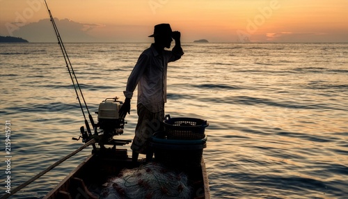 Silhouette of a fisherman standing beside a small boat engine while scanning the ocean for a productive fishing ground.