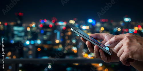Close up of person hands holding and using modern smartphone with blurred night city skyline bokeh lights in background