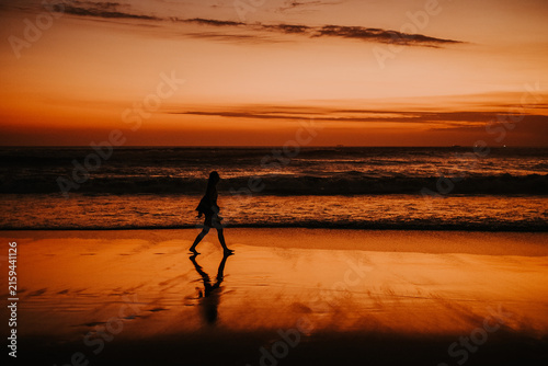 Fotografie Majestic seascape setting the sky ablaze as a silhouetted person walks along the