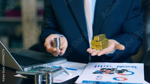 Businessman holding coins in one hand and gold bars in the other to compare investment assets and cash flow.