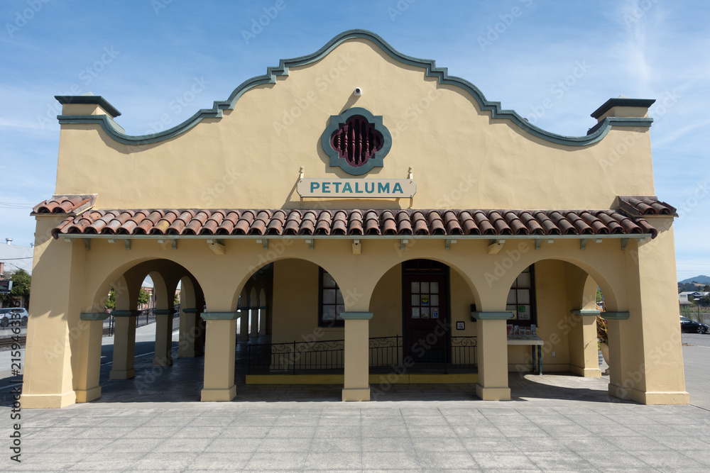 Obraz premium Historic Petaluma train station featuring Mission Revival architecture, arched colonnades, clay tile roofing, and the Petaluma name on the facade in Petaluma, California.