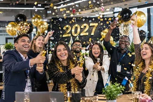 Diverse business team celebrating New Year 2027 with confetti in modern office workspace.